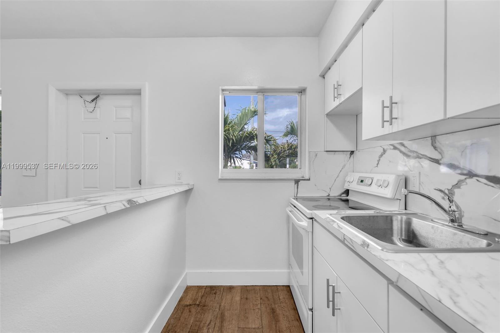 A kitchen features white cabinets, a marble-patterned countertop, and a window overlooking palm trees — 5549 NE Miami Ct # 1, Miami FL 33137, MIAMI, FL