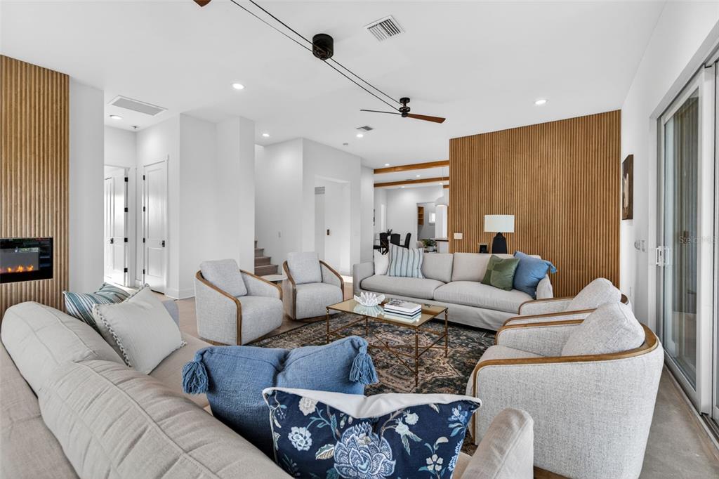 A living room features light-colored furniture, a glass coffee table, and wood-slatted accent walls — 3221 GULF BOULEVARD, BELLEAIR BEACH, FL
