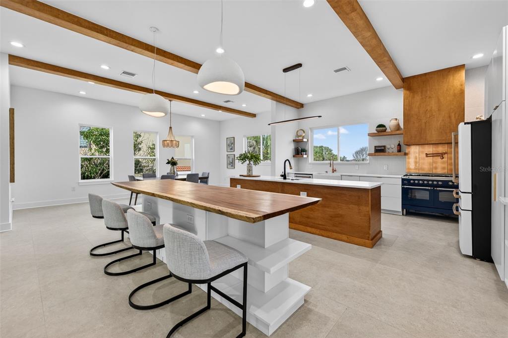 A modern kitchen features a live-edge wood island, white cabinetry, and exposed ceiling beams — 3221 GULF BOULEVARD, BELLEAIR BEACH, FL
