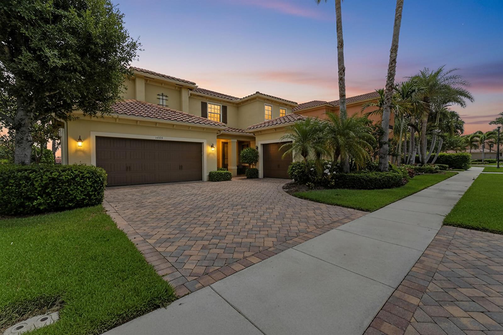 A two-story house with a paved driveway, two garages, and palm trees at dusk — 10519 Longleaf Lane, Wellington FL 33414, WELLINGTON, FL