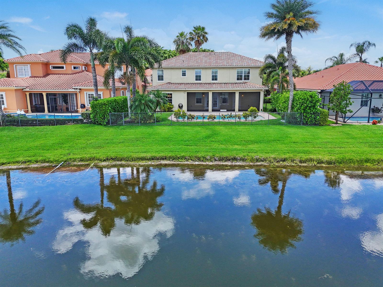 An aerial view shows three houses with tiled roofs, pools, and palm trees facing a lake — 10519 Longleaf Lane, Wellington FL 33414, WELLINGTON, FL