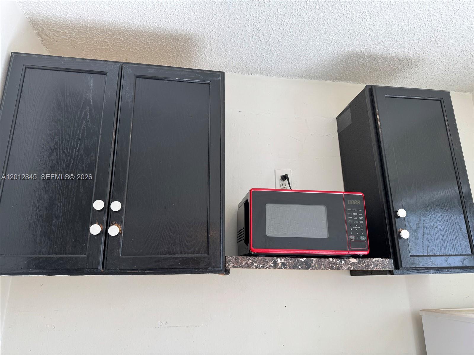 A red microwave sits on a small shelf between black kitchen cabinets — 1822 Cleveland St # 4, Hollywood FL 33020, HOLLYWOOD, FL