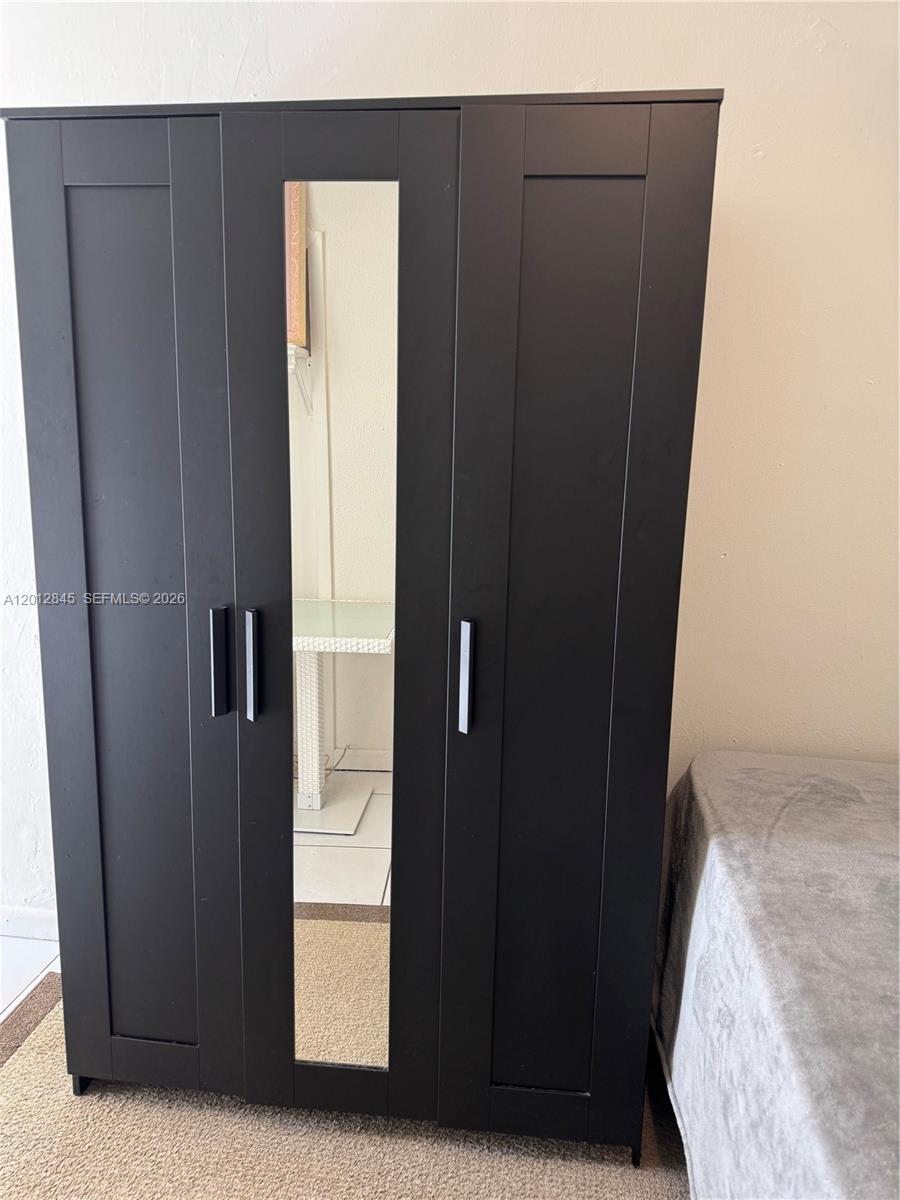 A black three-door wardrobe with a central mirror stands in a room — 1822 Cleveland St # 4, Hollywood FL 33020, HOLLYWOOD, FL