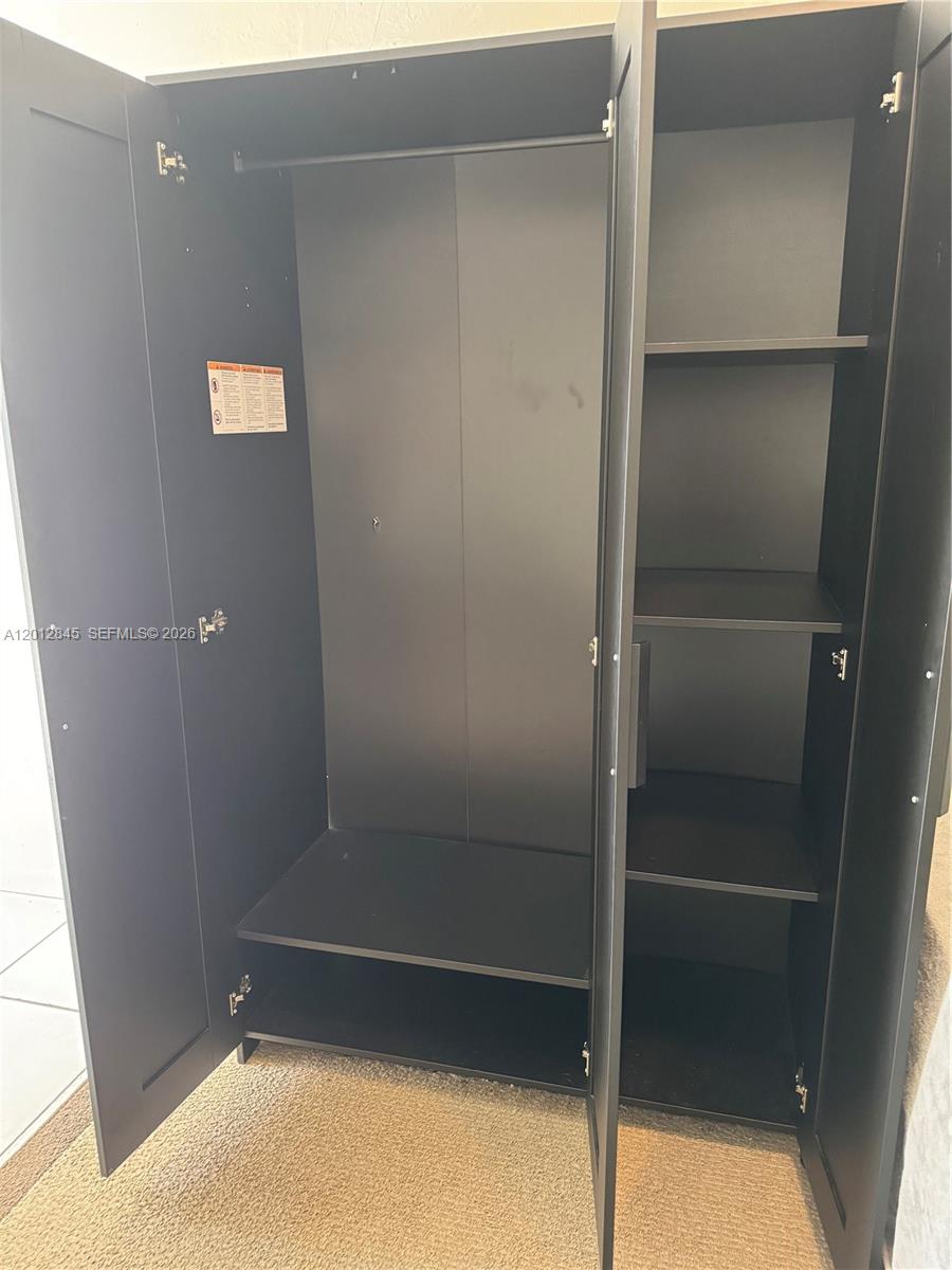 An open black wardrobe stands on a carpeted floor with hanging and shelf storage — 1822 Cleveland St # 4, Hollywood FL 33020, HOLLYWOOD, FL