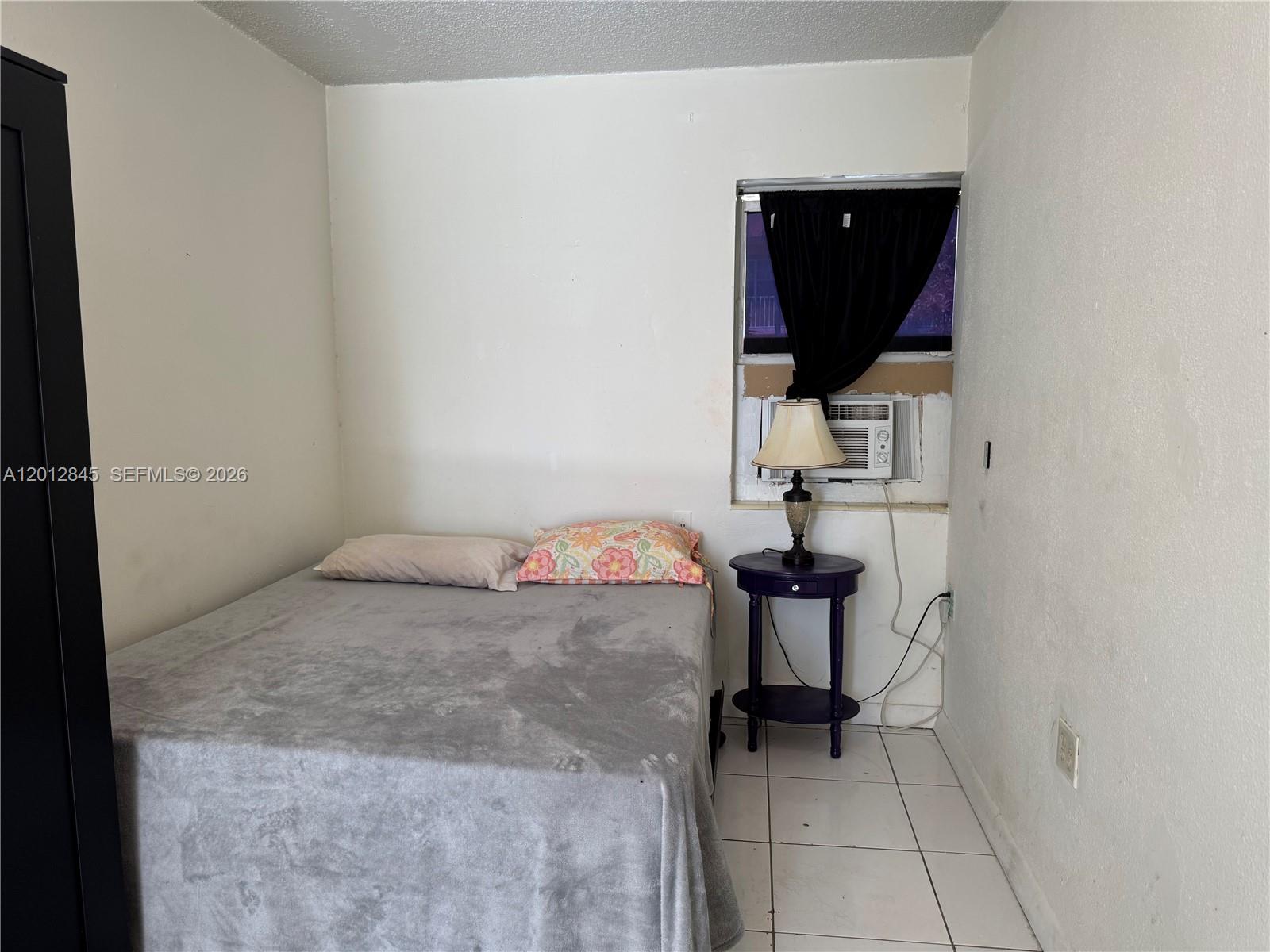A bedroom features a bed, a small purple side table with a lamp, and a window — 1822 Cleveland St # 4, Hollywood FL 33020, HOLLYWOOD, FL