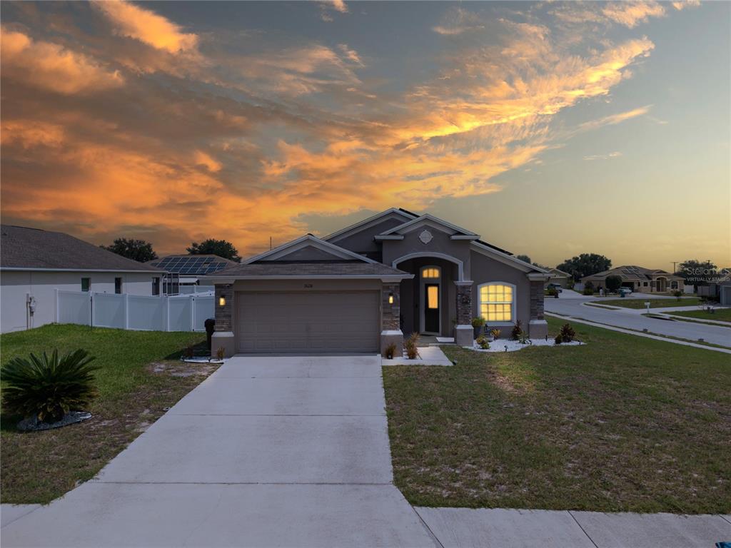 A single-story suburban house with a concrete driveway and a sunset sky in the background — 2628 SUNSET CIRCLE, LAKE WALES, FL