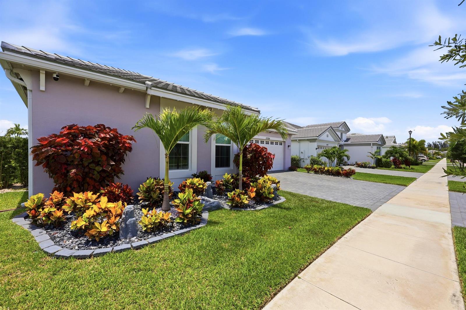 A light purple house with a paved driveway and landscaped front yard under a blue sky — 15264 Wildwood Circle, Westlake FL 33470, WESTLAKE, FL