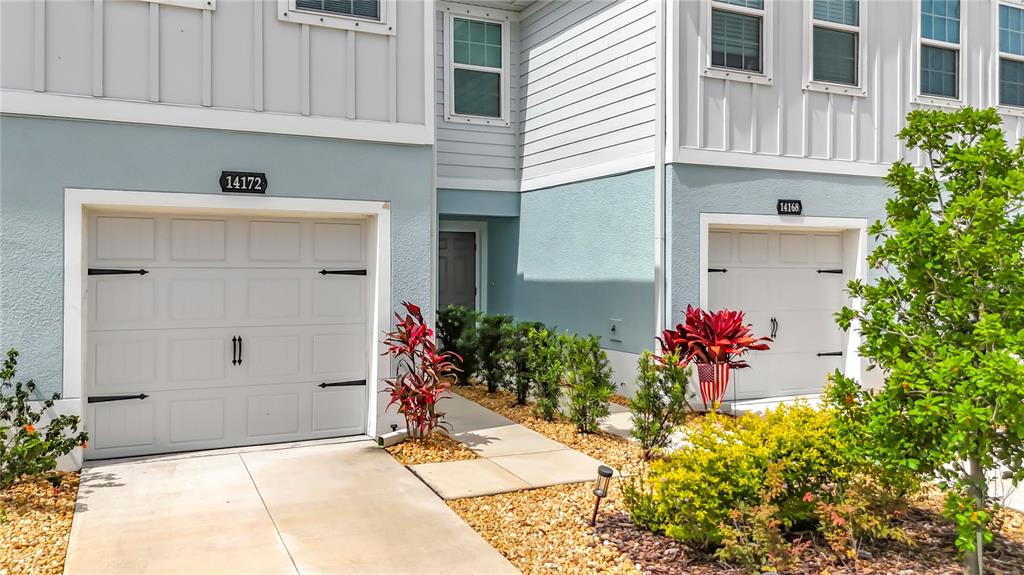 The exterior of two adjacent townhomes features light blue siding, white garage doors, and landscaping — 14172 CRIMSON AVENUE, BRADENTON, FL