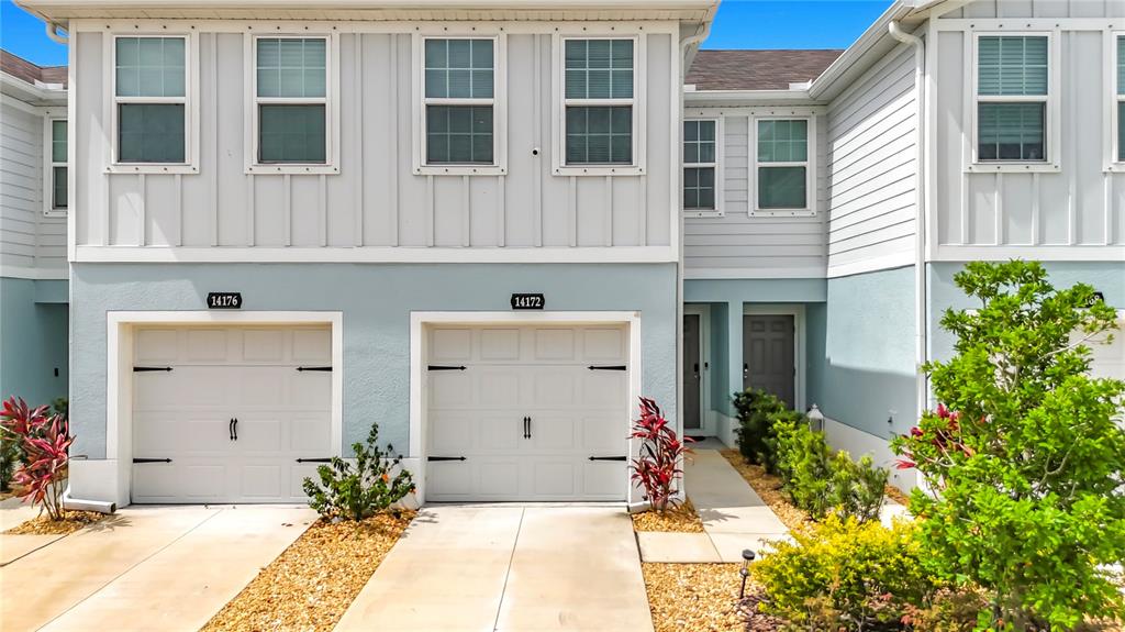 The exterior of a two-story townhouse features light blue stucco, white vertical siding, and two garages — 14172 CRIMSON AVENUE, BRADENTON, FL