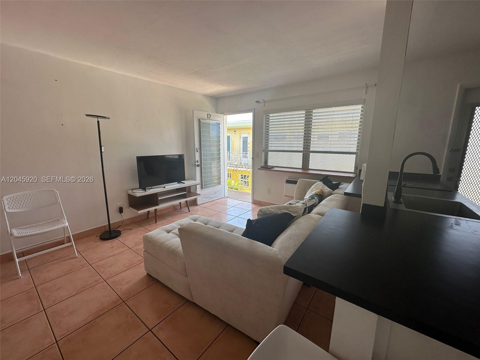 A living room features tile floors, a sectional sofa, a television, and an exterior door — 8101 Abbott Ave # 17, Miami Beach FL 33141, MIAMI BEACH, FL