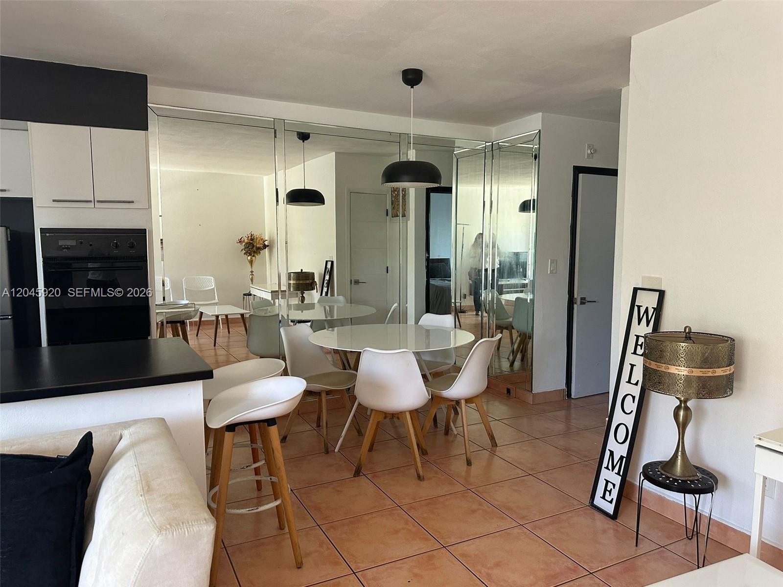 A dining area with a round table, white chairs, mirrored walls, and tile flooring — 8101 Abbott Ave # 17, Miami Beach FL 33141, MIAMI BEACH, FL