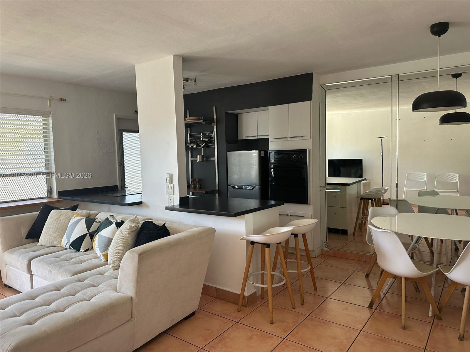 An open-concept living area features a white sectional sofa, kitchen peninsula, and dining space — 8101 Abbott Ave # 17, Miami Beach FL 33141, MIAMI BEACH, FL