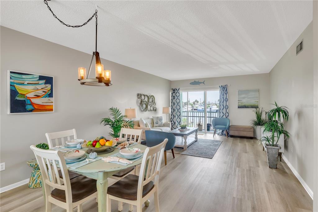 An open-concept living and dining area features light wood flooring, a chandelier, and balcony access — 715 S BEACH STREET UNIT 211D, DAYTONA BEACH, FL