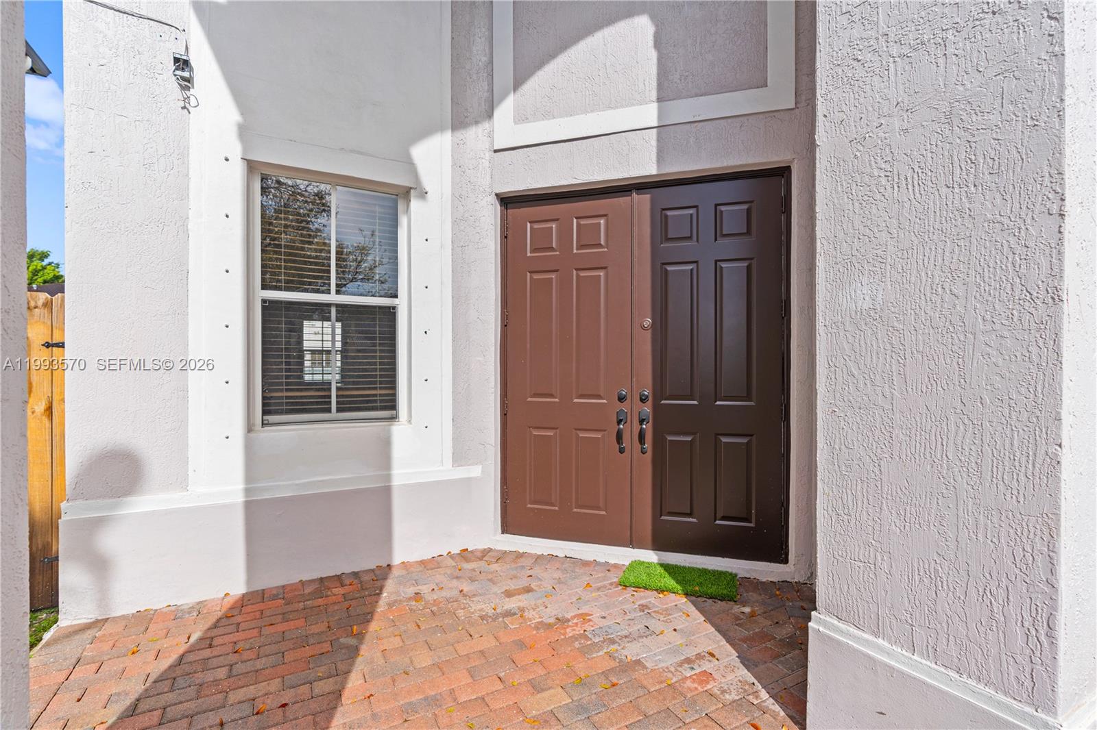 A brick patio leads to a set of brown double doors next to a window — 18140 NW 90th Ave, Hialeah FL 33018, HIALEAH, FL