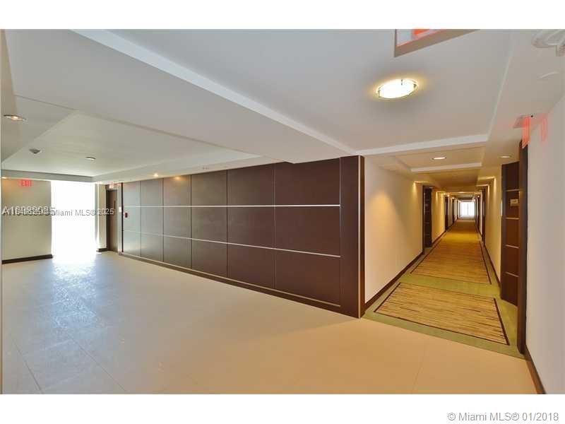 A long hallway features dark wood paneling, recessed lighting, and a carpeted floor — 5701 Collins Ave # 1008, Miami Beach FL 33140, MIAMI BEACH, FL