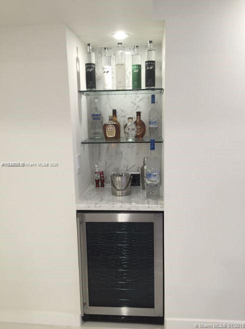 A built-in wet bar features glass shelving, marble backing, and a stainless steel wine refrigerator — 5701 Collins Ave # 1008, Miami Beach FL 33140, MIAMI BEACH, FL