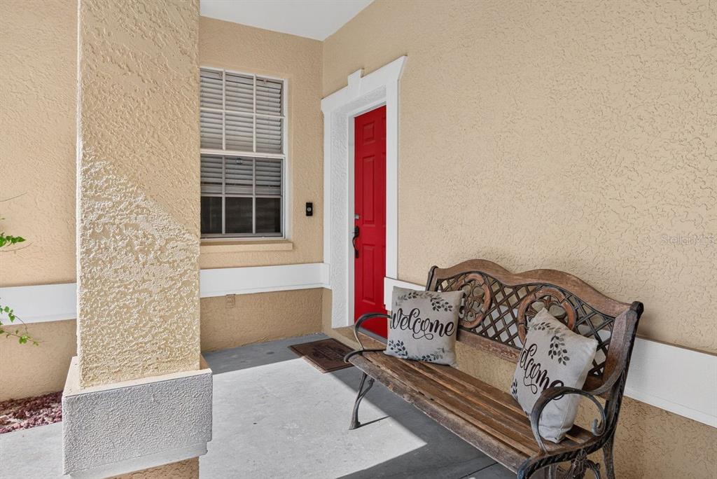 A covered front porch features a red door, a metal bench, and beige stucco walls — 648 SPRING LAKE CIRCLE, TARPON SPRINGS, FL