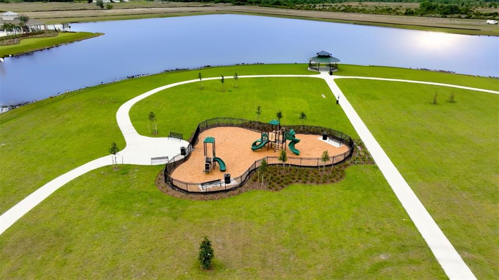 An aerial view of a fenced playground with slides and swings near a lake — 3499 MALAWI TRAIL, ST CLOUD, FL