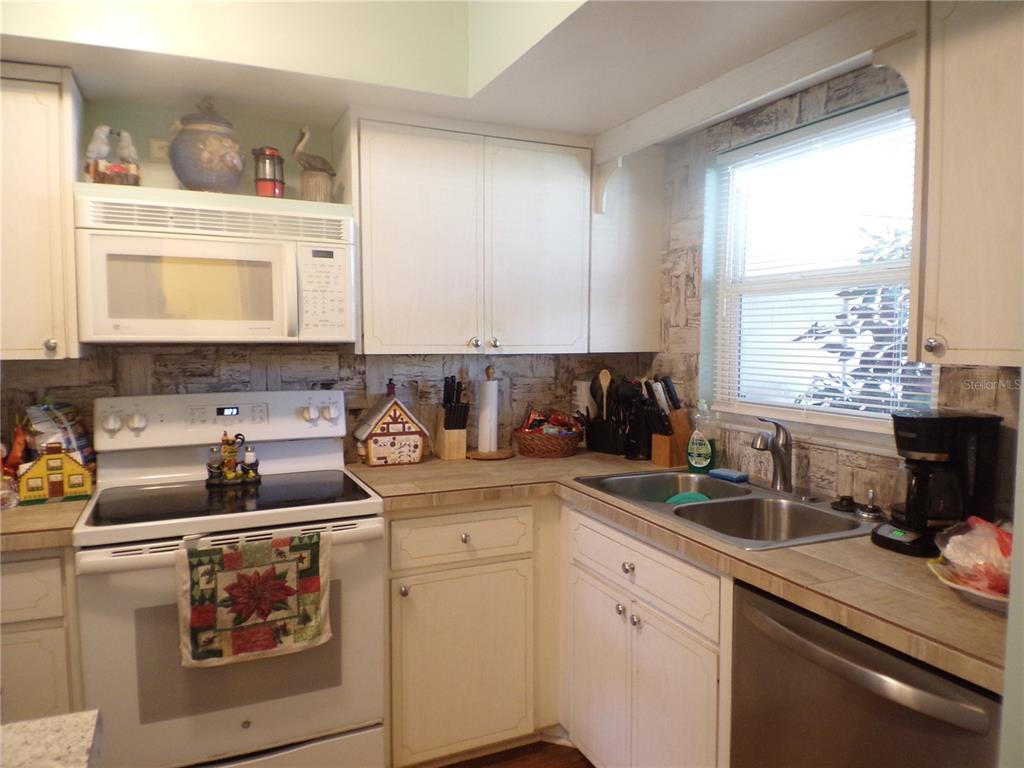 A kitchen features white cabinets, a white stove, a stainless steel dishwasher, and tiled countertops — 670 PARK CIRCLE, BRADENTON, FL