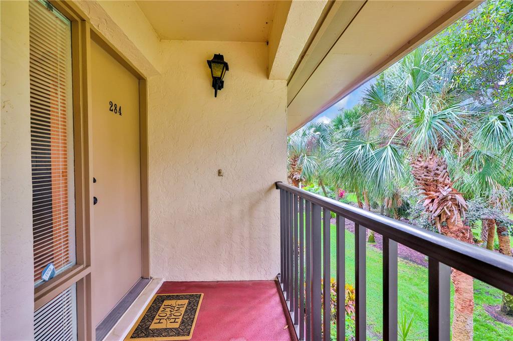 An exterior apartment balcony features a tan door, a welcome mat, and a metal railing — 3450 WOOD OWL CIRCLE UNIT 284, BRADENTON, FL
