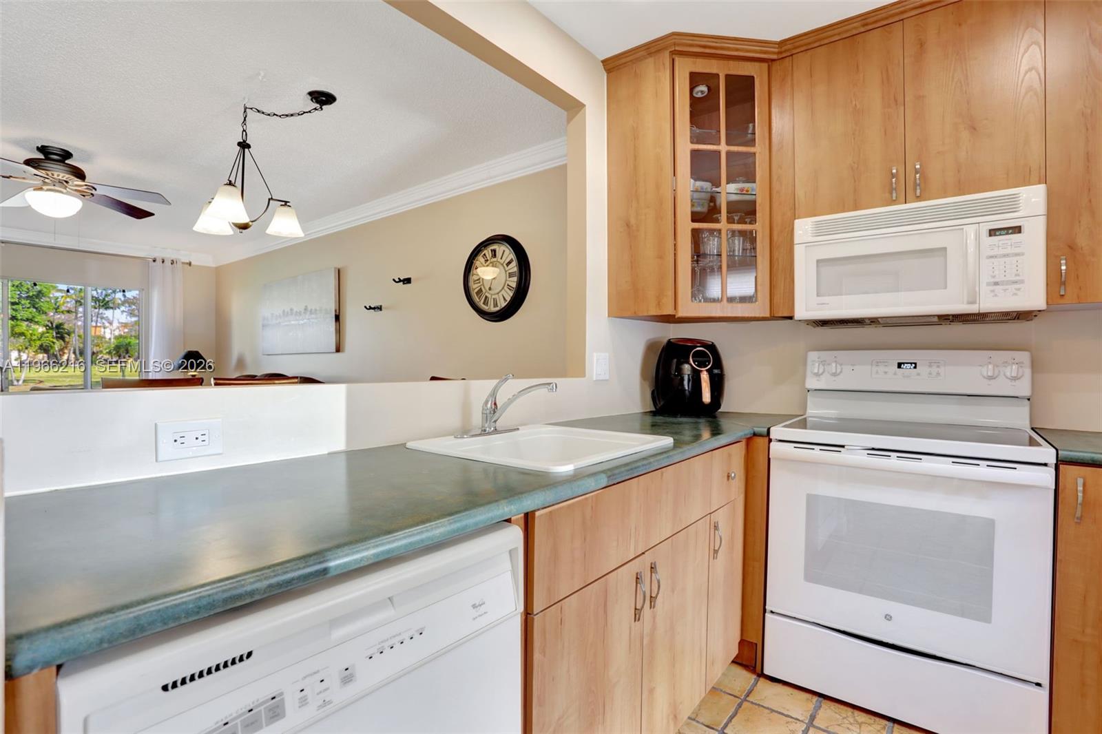 A kitchen features light wood cabinets, green countertops, white appliances, and a pass-through to the living area — 4311 NW 16th St # B103, Lauderhill FL 33313, LAUDERHILL, FL