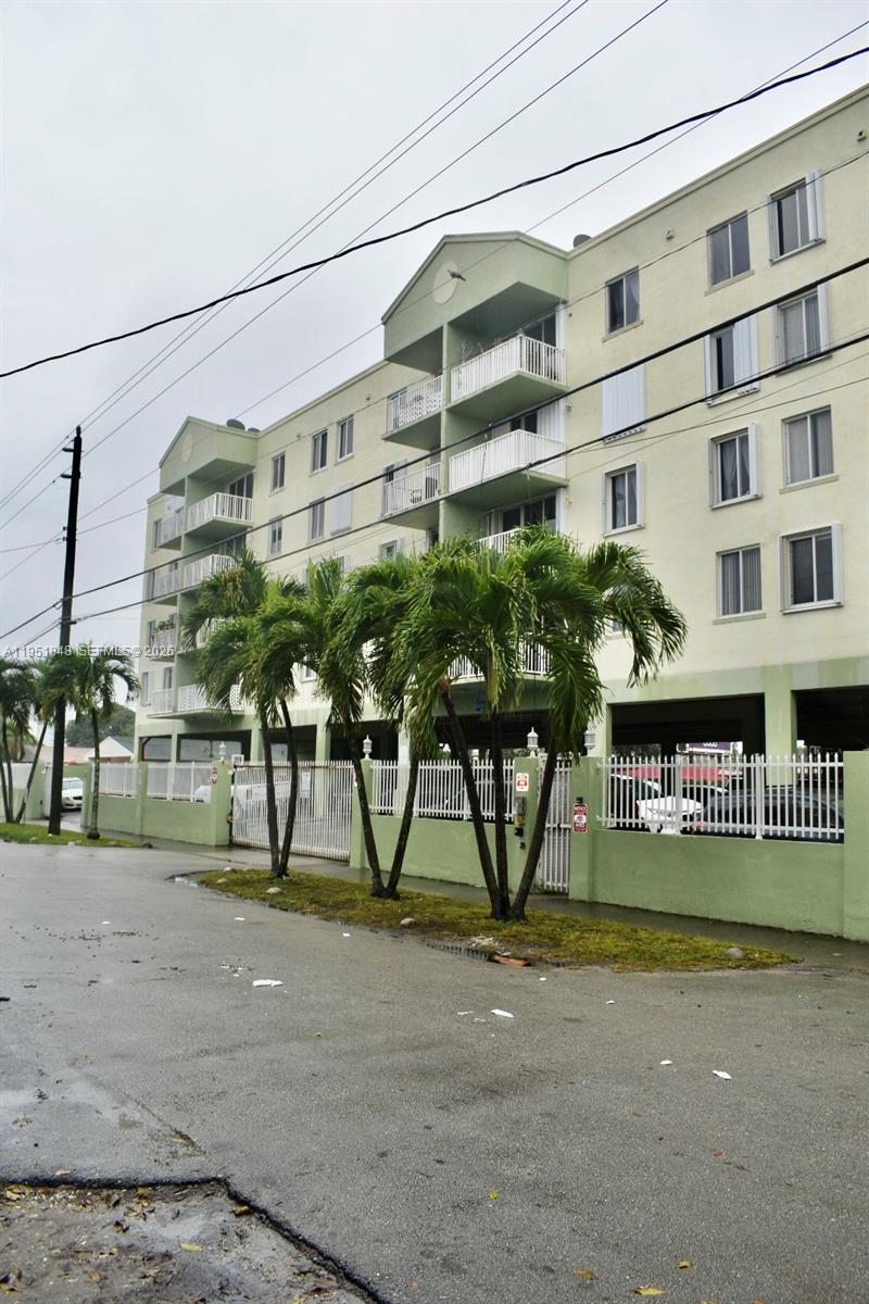 A multi-story apartment building with balconies and a gated parking area sits behind palm trees — 616 NW 26th Ave # 210, Miami FL 33125, MIAMI, FL