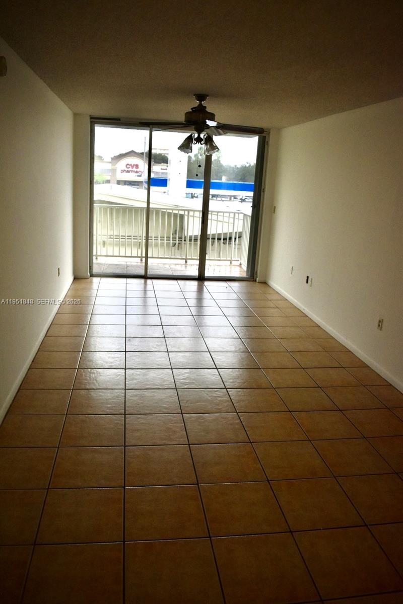 An empty room features beige tile flooring, a ceiling fan, and a sliding glass balcony door — 616 NW 26th Ave # 210, Miami FL 33125, MIAMI, FL
