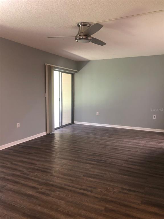 A living room with gray walls, dark wood-look flooring, a ceiling fan, and sliding glass doors — 170 PALMETTO WOODS COURT UNIT 3C, DELTONA, FL