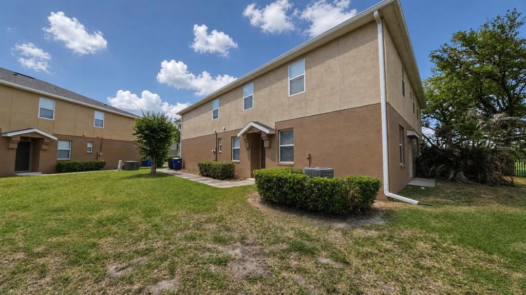 A two-story tan and brown stucco townhouse exterior with a small lawn and bushes — 4116 ORANGE TREE COURT, ST CLOUD, FL