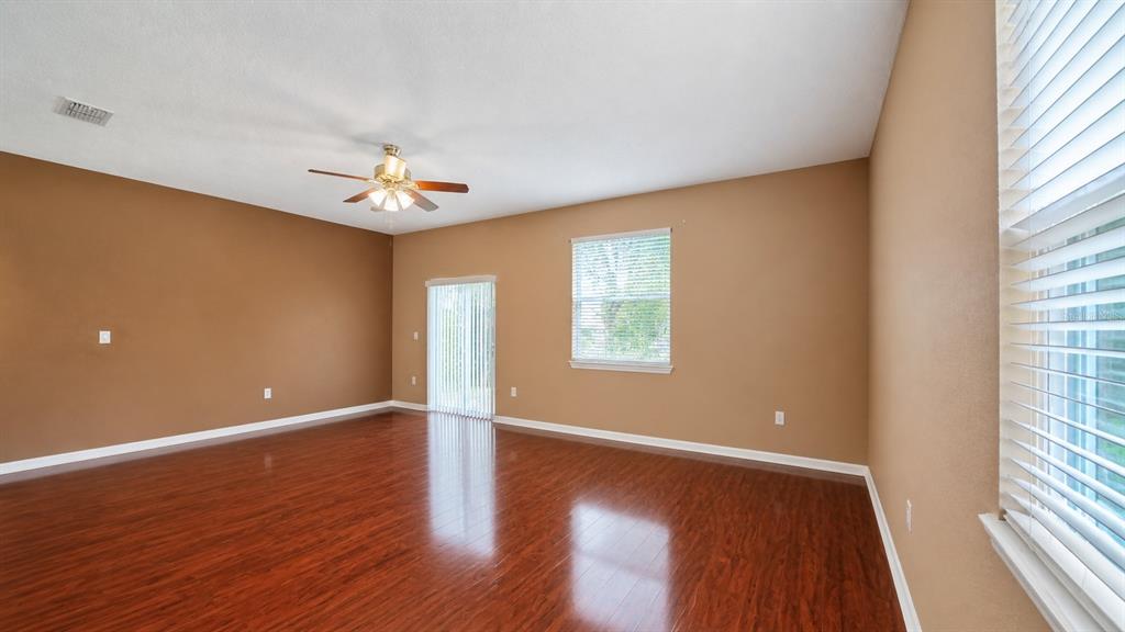 An empty room features brown walls, dark wood-look flooring, a ceiling fan, and sliding doors — 4116 ORANGE TREE COURT, ST CLOUD, FL