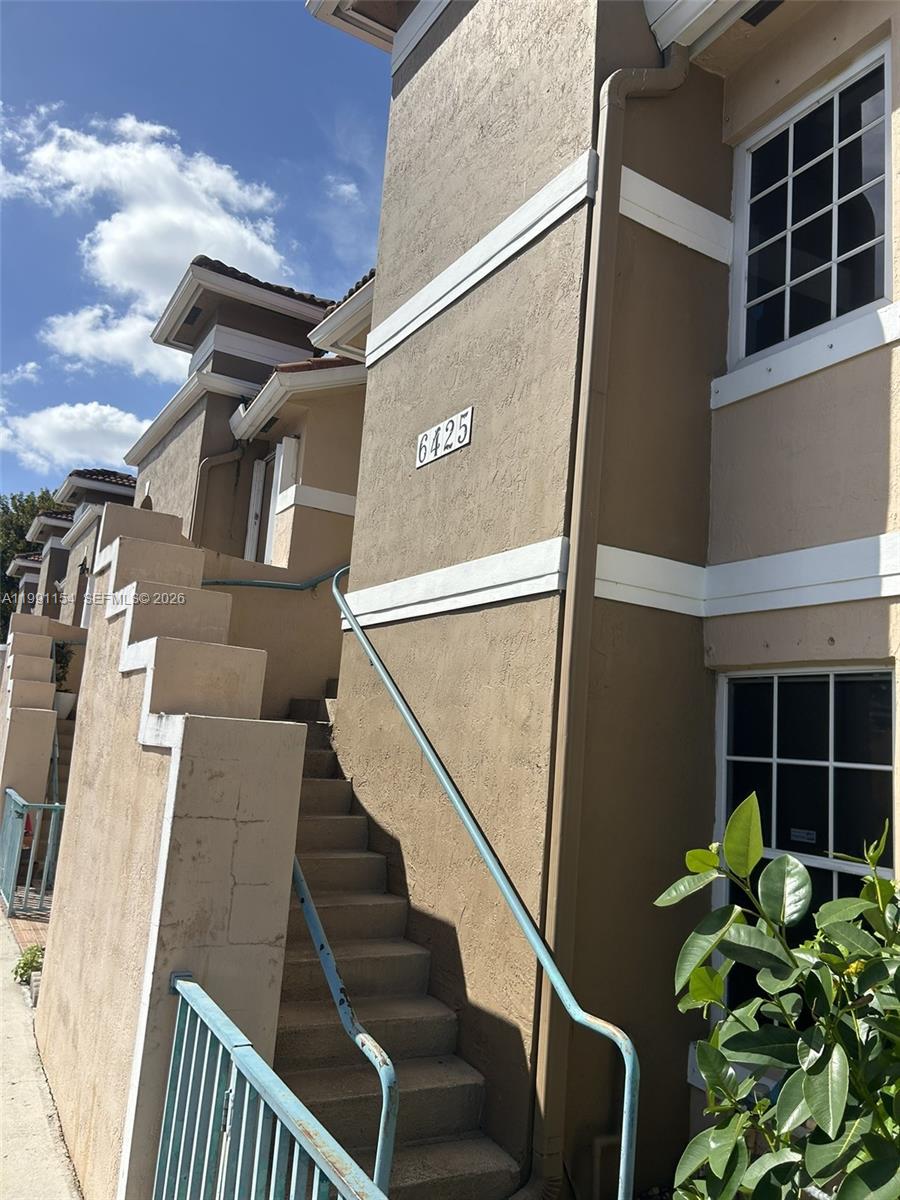 An exterior view shows a tan building with a staircase leading to an upper level — 6425 SW 130th Pl # 704, Miami FL 33183, MIAMI, FL