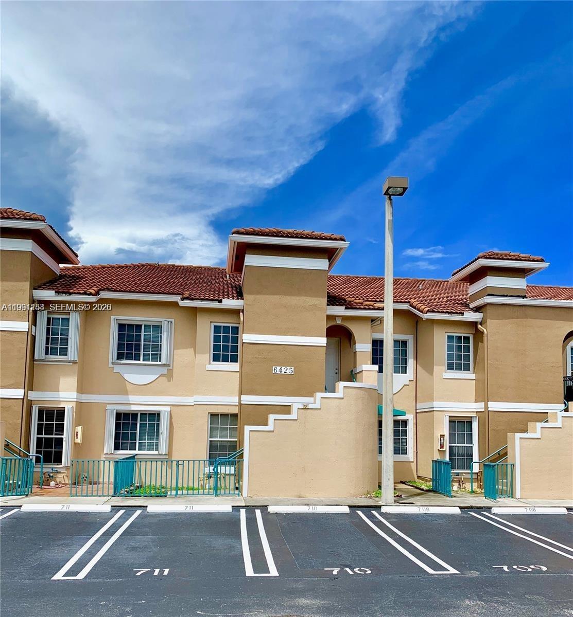A two-story tan apartment building features a red tile roof and designated parking spaces — 6425 SW 130th Pl # 704, Miami FL 33183, MIAMI, FL