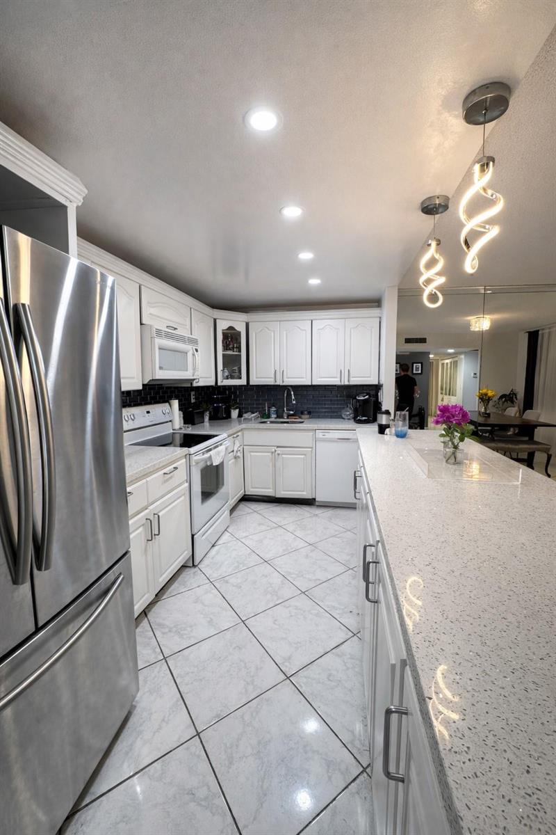 A kitchen features white cabinets, stainless steel appliances, a quartz island, and light tile flooring — 20441 NE 30th Avenue # 9, Miami FL 33180, MIAMI, FL