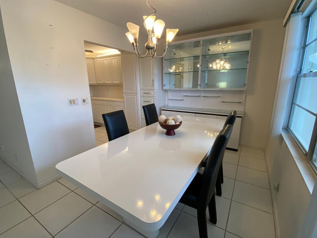 A dining room features a white table, black chairs, a glass-front hutch, and tile flooring — 3043 Berkshire C, Deerfield Beach FL 33442, DEERFIELD BEACH, FL