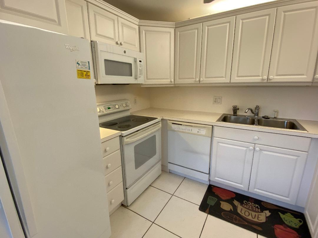 A kitchen features white cabinets, white appliances, a double sink, and tiled flooring — 3043 Berkshire C, Deerfield Beach FL 33442, DEERFIELD BEACH, FL