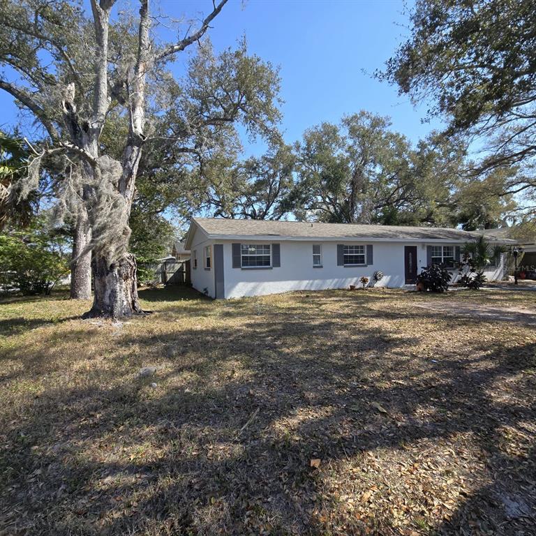 A single-story white house with dark shutters sits on a lot with large trees — 1021 FAIRBURN AVENUE, CLEARWATER, FL