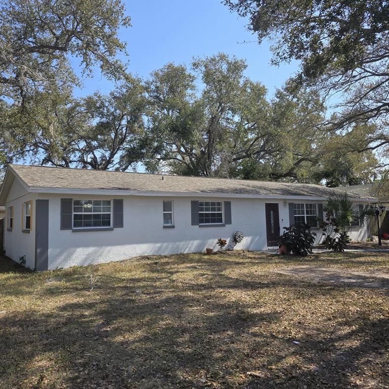 A single-story white house with gray shutters and a shingled roof under large trees — 1021 FAIRBURN AVENUE, CLEARWATER, FL