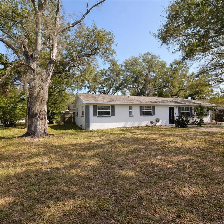 A single-story white house with dark shutters sits on a grassy lot with large trees — 1021 FAIRBURN AVENUE, CLEARWATER, FL