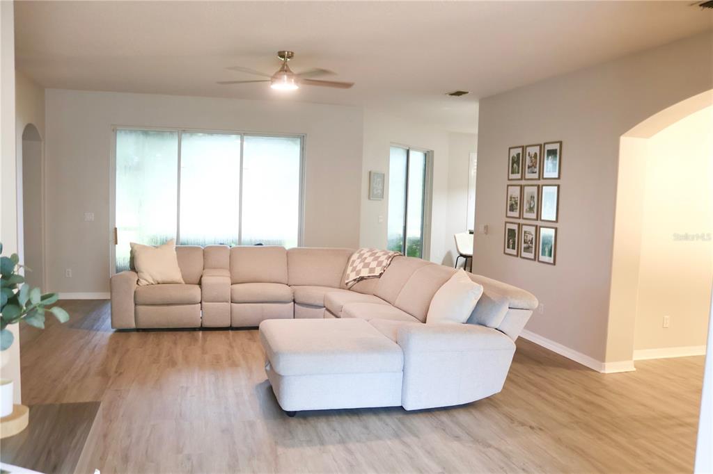 A living room features a large beige sectional sofa, light wood flooring, and a ceiling fan — 3850 BEACON RIDGE WAY, CLERMONT, FL