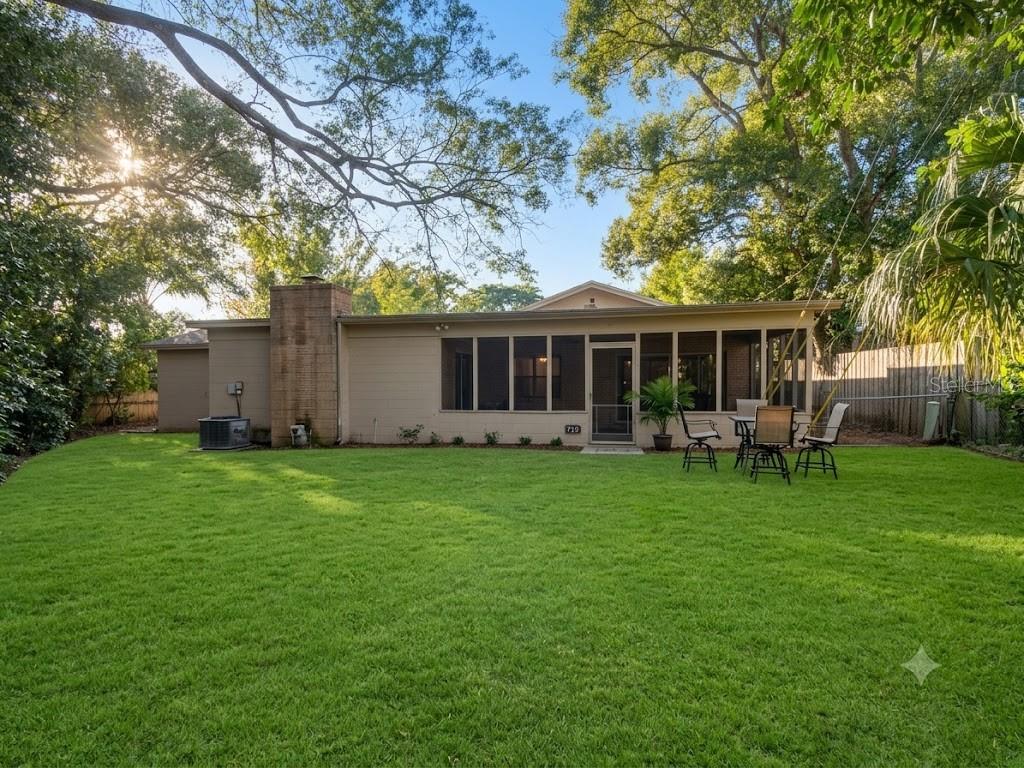 A backyard with a green lawn, large trees, and a house with a screened-in porch — 719 KEWANNEE TRAIL, MAITLAND, FL