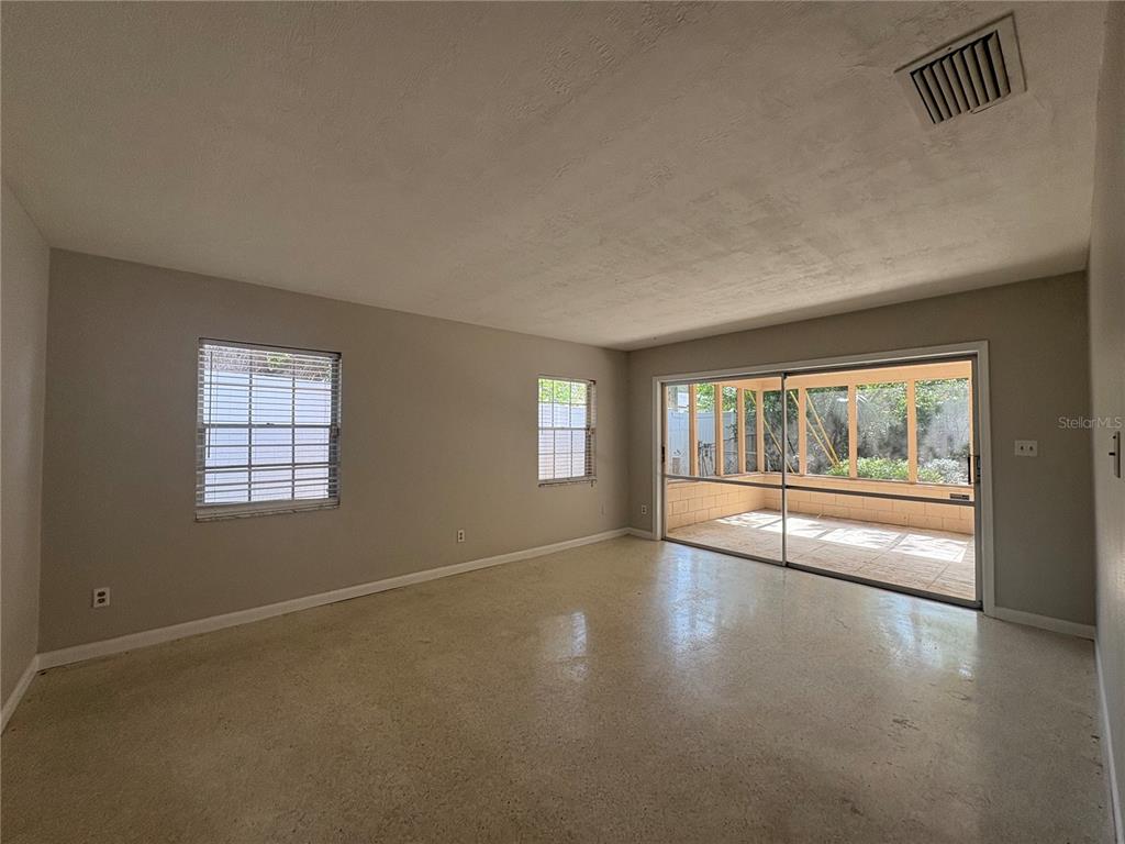 A living room with light walls, terrazzo flooring, two windows, and a sliding glass door — 719 KEWANNEE TRAIL, MAITLAND, FL