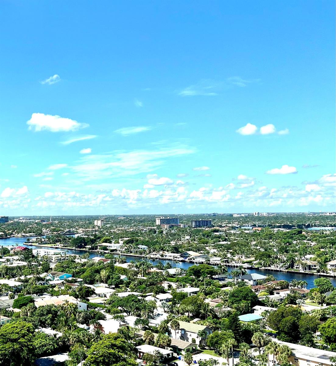 An aerial view shows a residential neighborhood with a canal and scattered buildings under blue skies — 111 Briny Avenue # 06, Pompano Beach FL 33062, POMPANO BEACH, FL