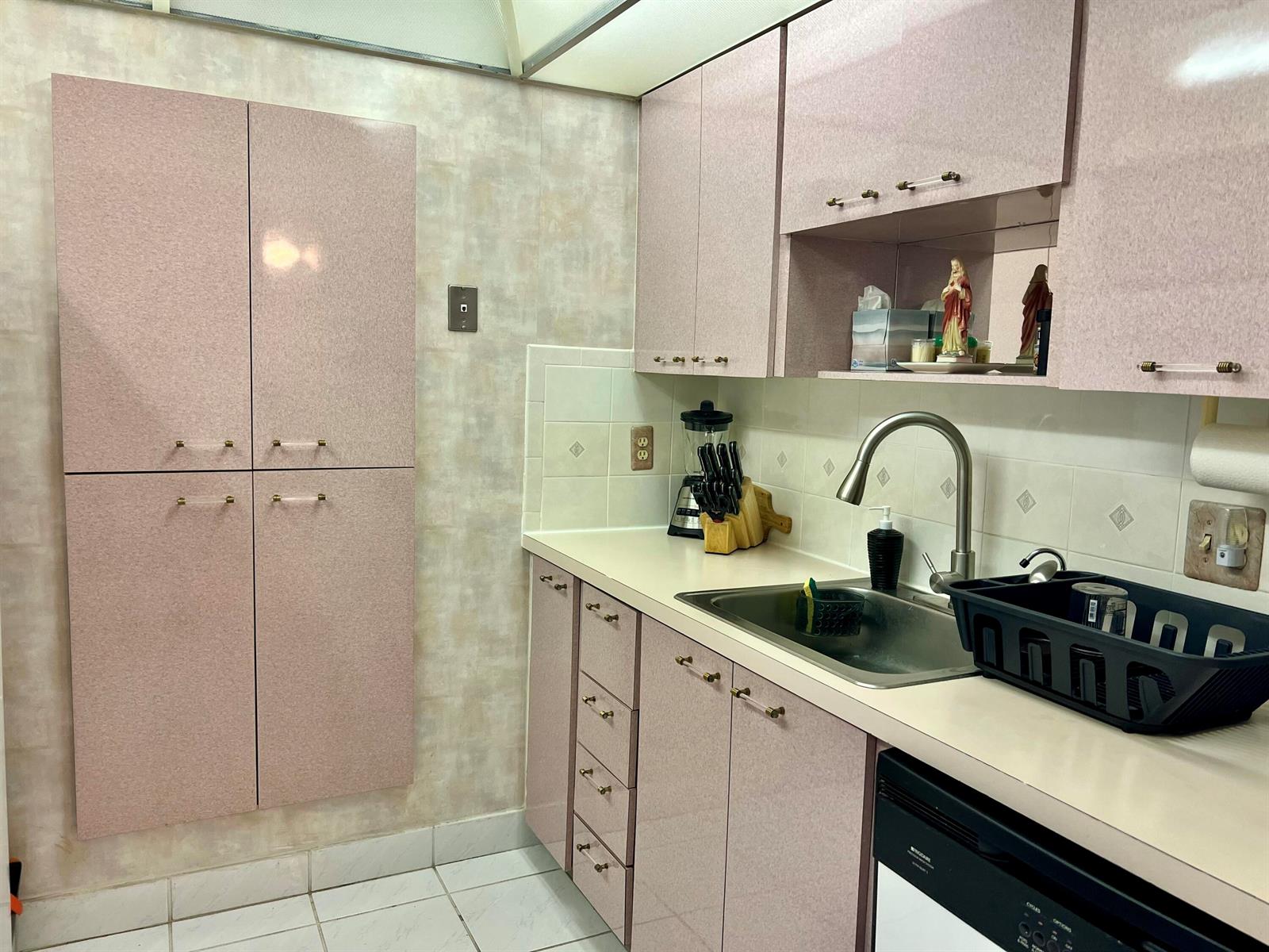 A kitchen features pink cabinets, a stainless steel sink, and light-colored tile flooring and backsplash — 111 Briny Avenue # 06, Pompano Beach FL 33062, POMPANO BEACH, FL