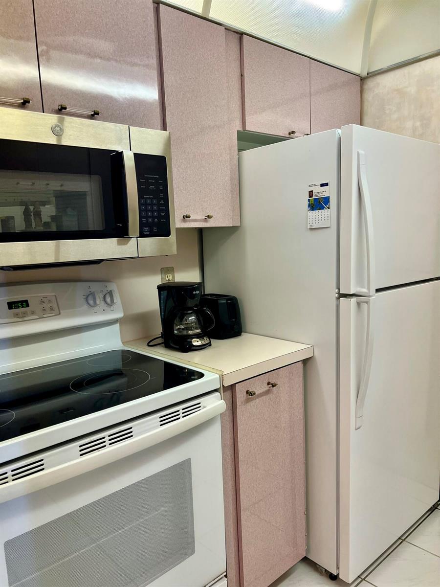 A kitchen features pink cabinets, white appliances, and a black coffee maker on the counter — 111 Briny Avenue # 06, Pompano Beach FL 33062, POMPANO BEACH, FL