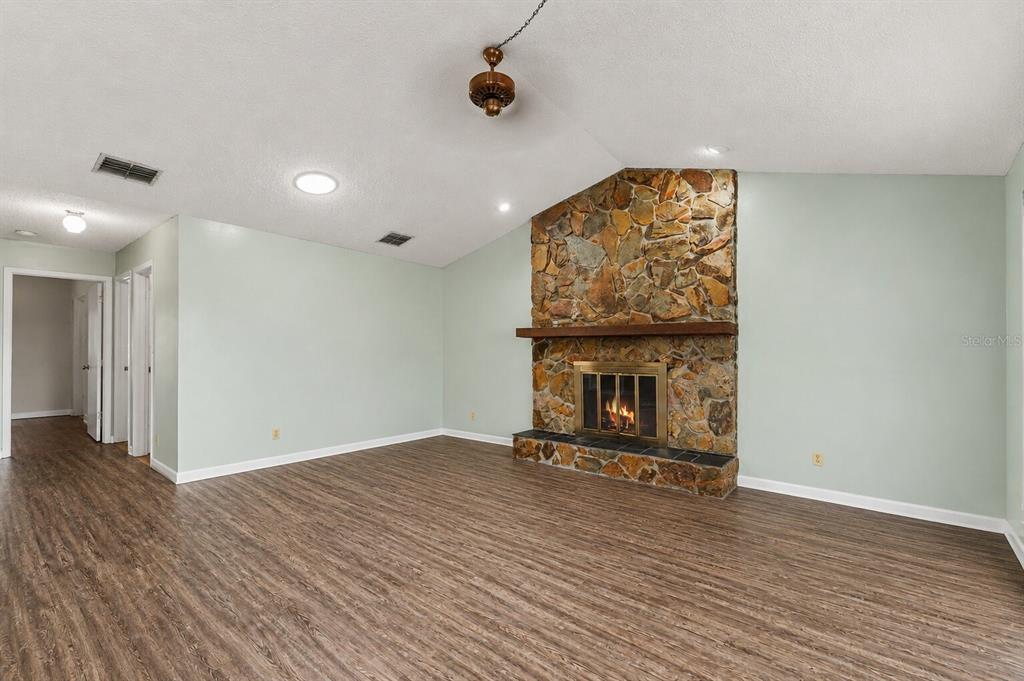 A living room features a stone fireplace, vaulted ceilings, and wood-look flooring — 9074 HEATHER BOULEVARD, WEEKI WACHEE, FL