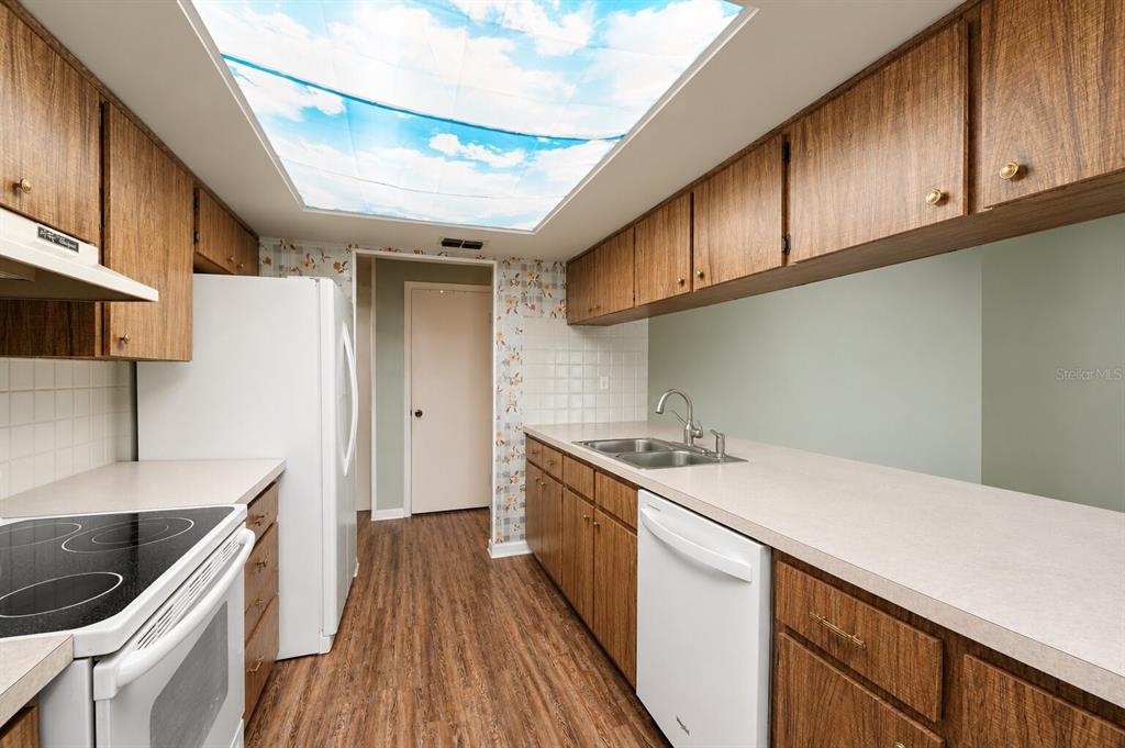 A kitchen features wood cabinets, white appliances, a sky-patterned ceiling panel, and laminate countertops — 9074 HEATHER BOULEVARD, WEEKI WACHEE, FL