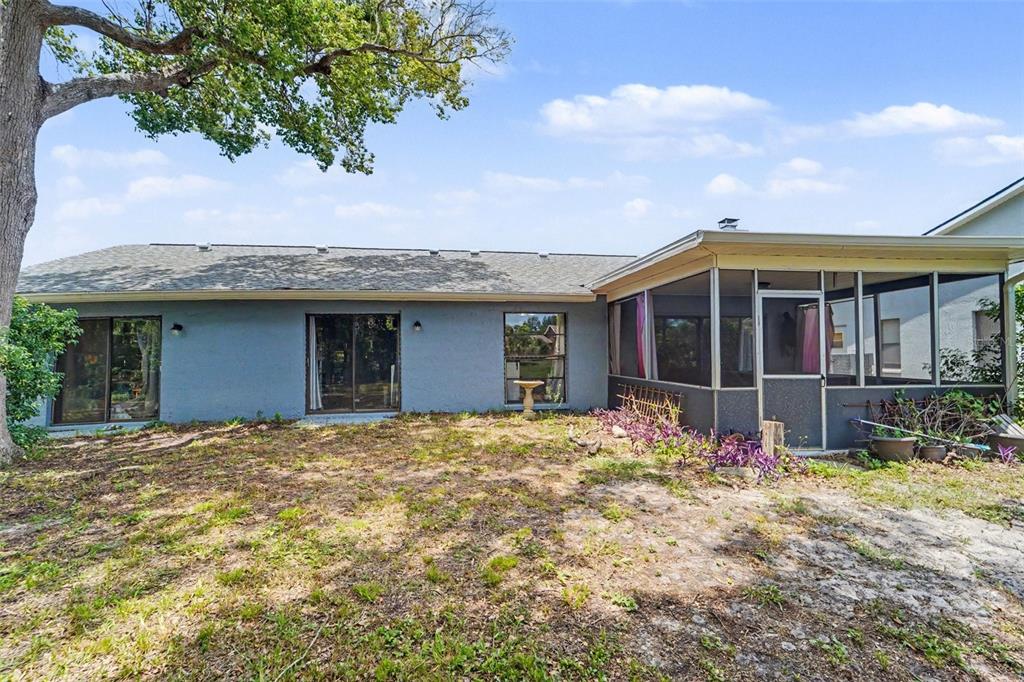 The rear exterior of a single-story house features a screened-in porch and sliding glass doors — 9074 HEATHER BOULEVARD, WEEKI WACHEE, FL