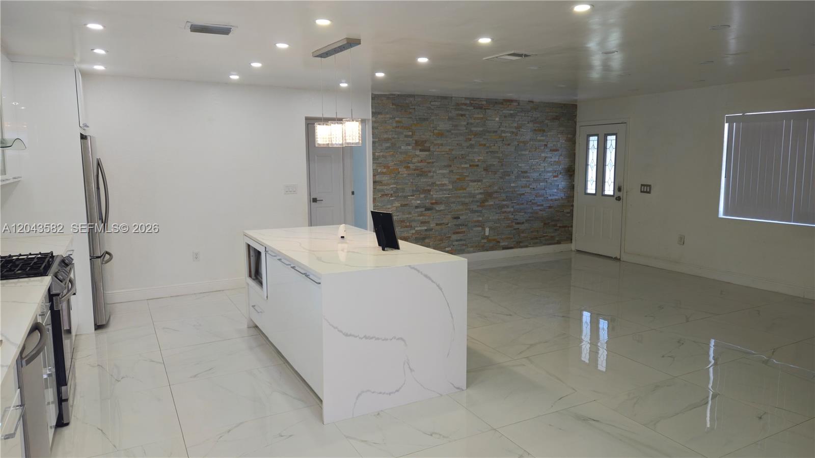 A modern kitchen features a marble-topped island, white cabinetry, and a stone accent wall — 12341 NW 30th St, Sunrise FL 33323, SUNRISE, FL