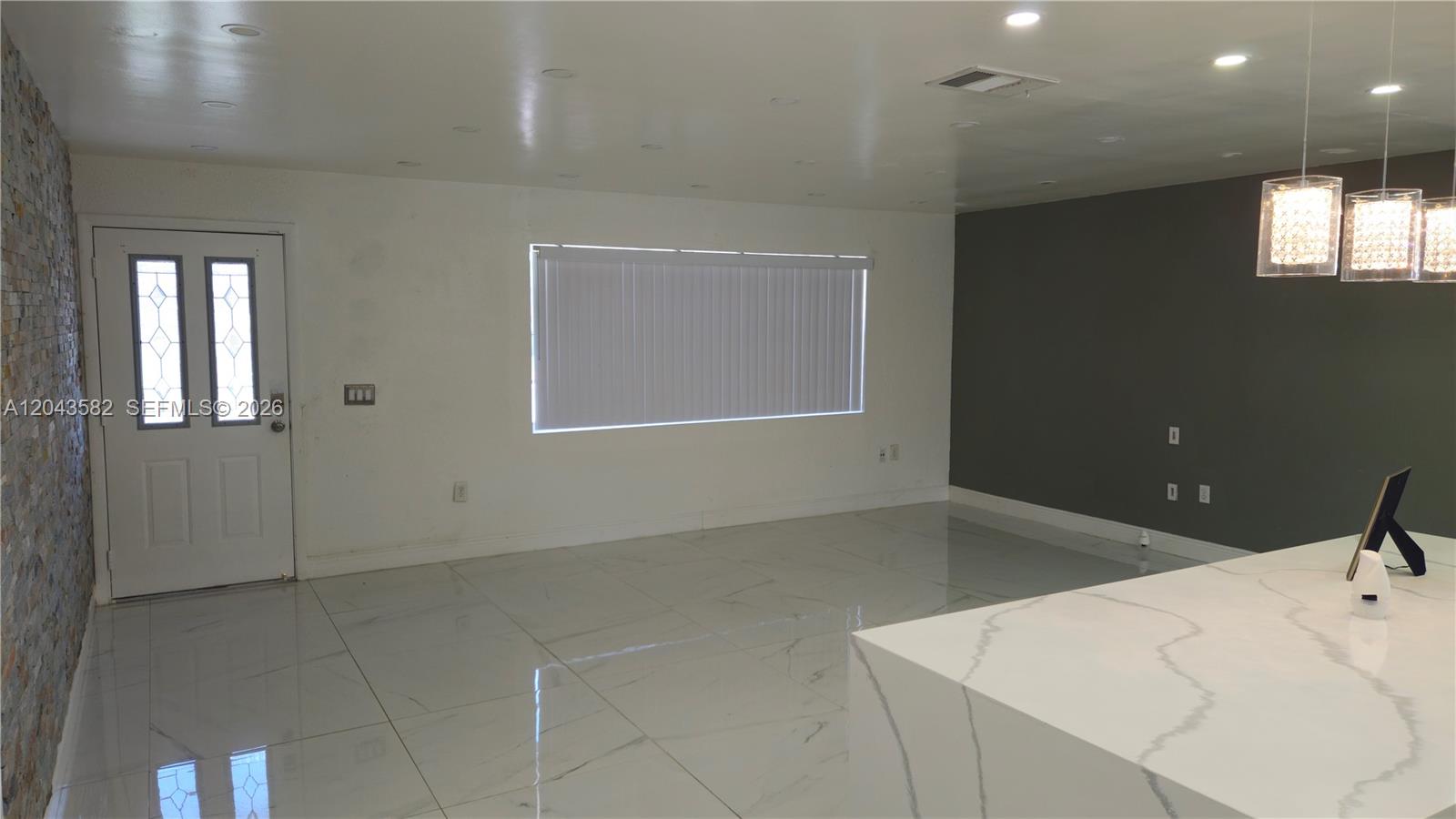 A bright room features white tile floors, a stone accent wall, and a kitchen island — 12341 NW 30th St, Sunrise FL 33323, SUNRISE, FL