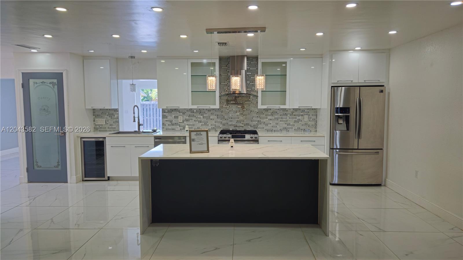 A modern kitchen features white cabinets, a dark island, stainless steel appliances, and tiled floors — 12341 NW 30th St, Sunrise FL 33323, SUNRISE, FL